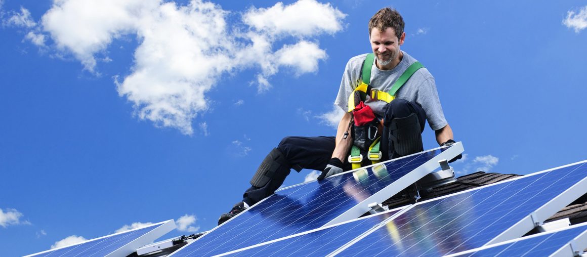 Рабочий устанавливает фотоэлектрические солнечные батареи альтернативной энергии на крыше