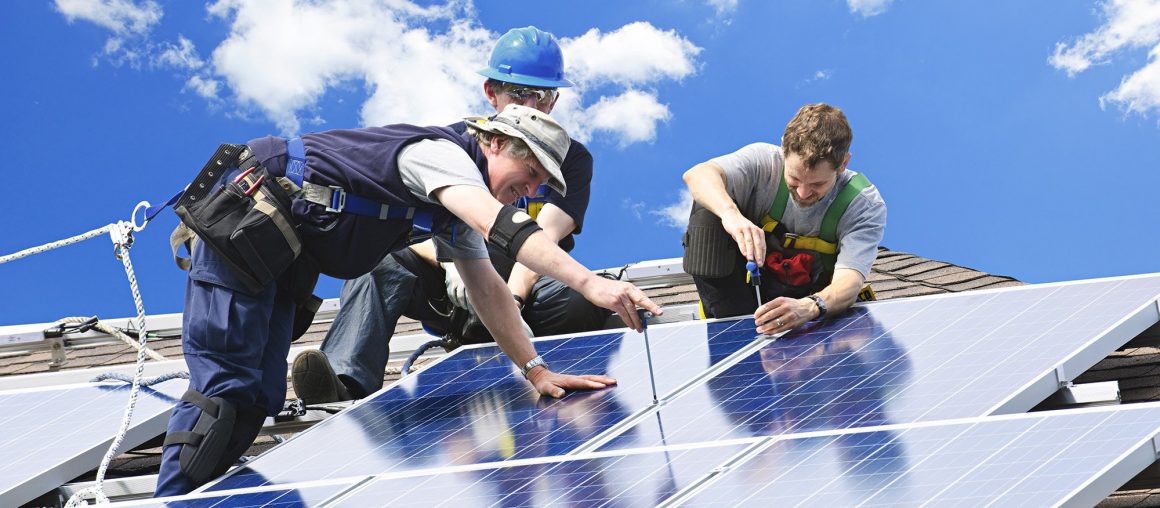 Работники, устанавливающие фотоэлектрические солнечные батареи альтернативной энергетики на крышах зданий